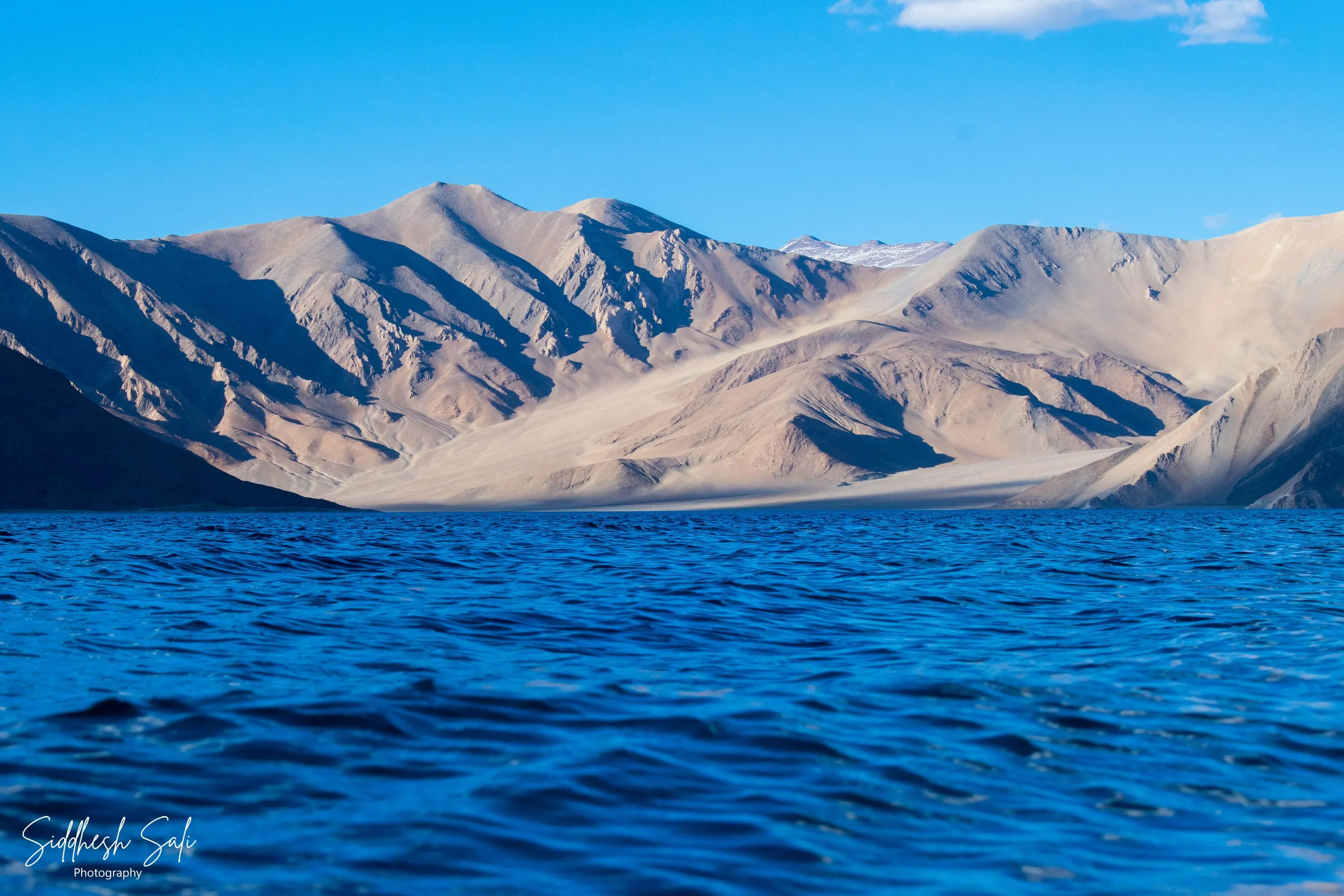 Deep blue water in the foreground running to a long bare ridge under a bright sky.