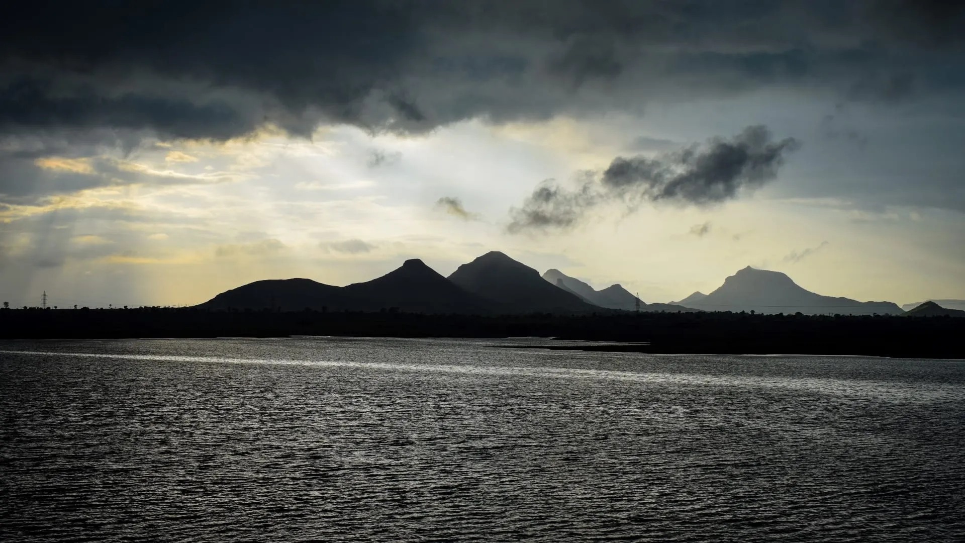 A dark lake below a heavy grey cloudbank, with low hills strung along the horizon.