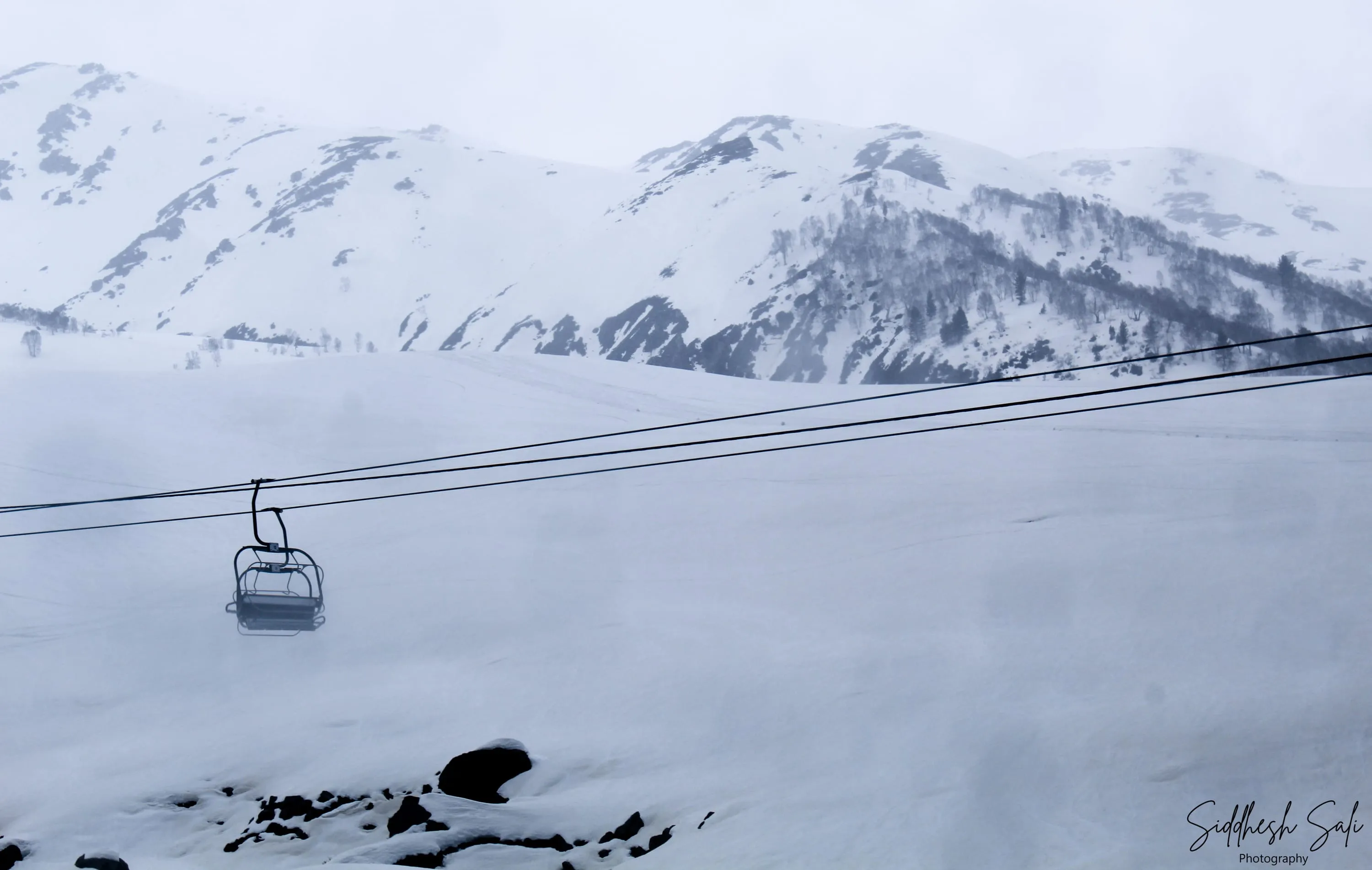 An empty gondola cable car crossing a snowfield, mountains flattened into white behind it.