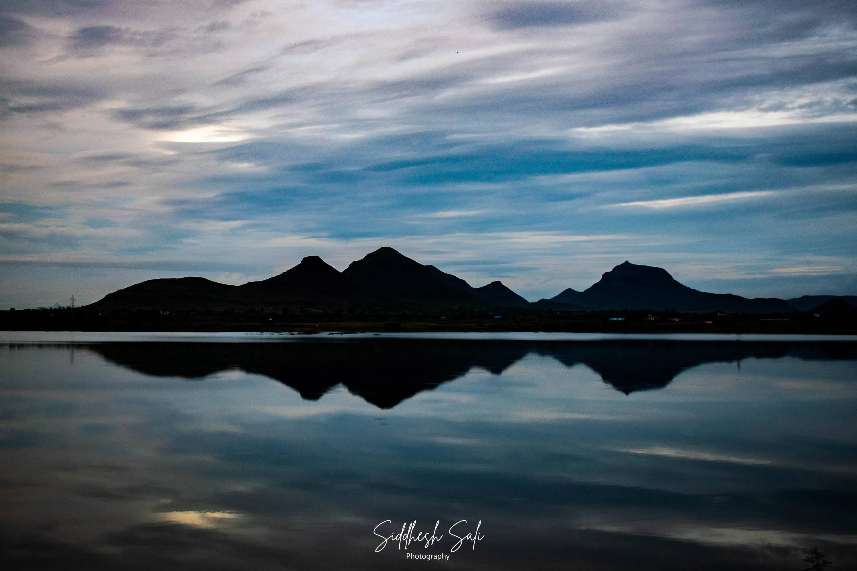 Low hills and streaked cloud reflected in perfectly flat water at blue hour.