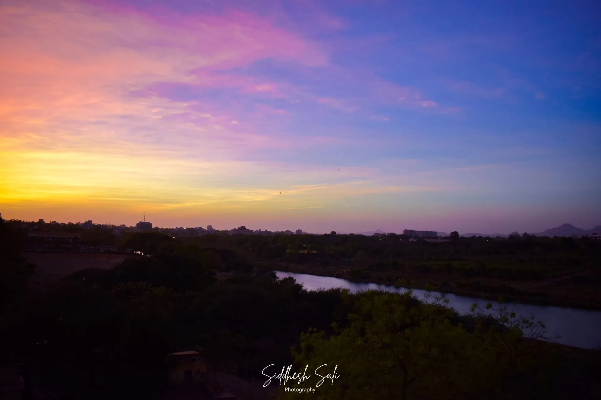 A river at dusk under a sky graded from pink to deep blue, trees dark along both banks.