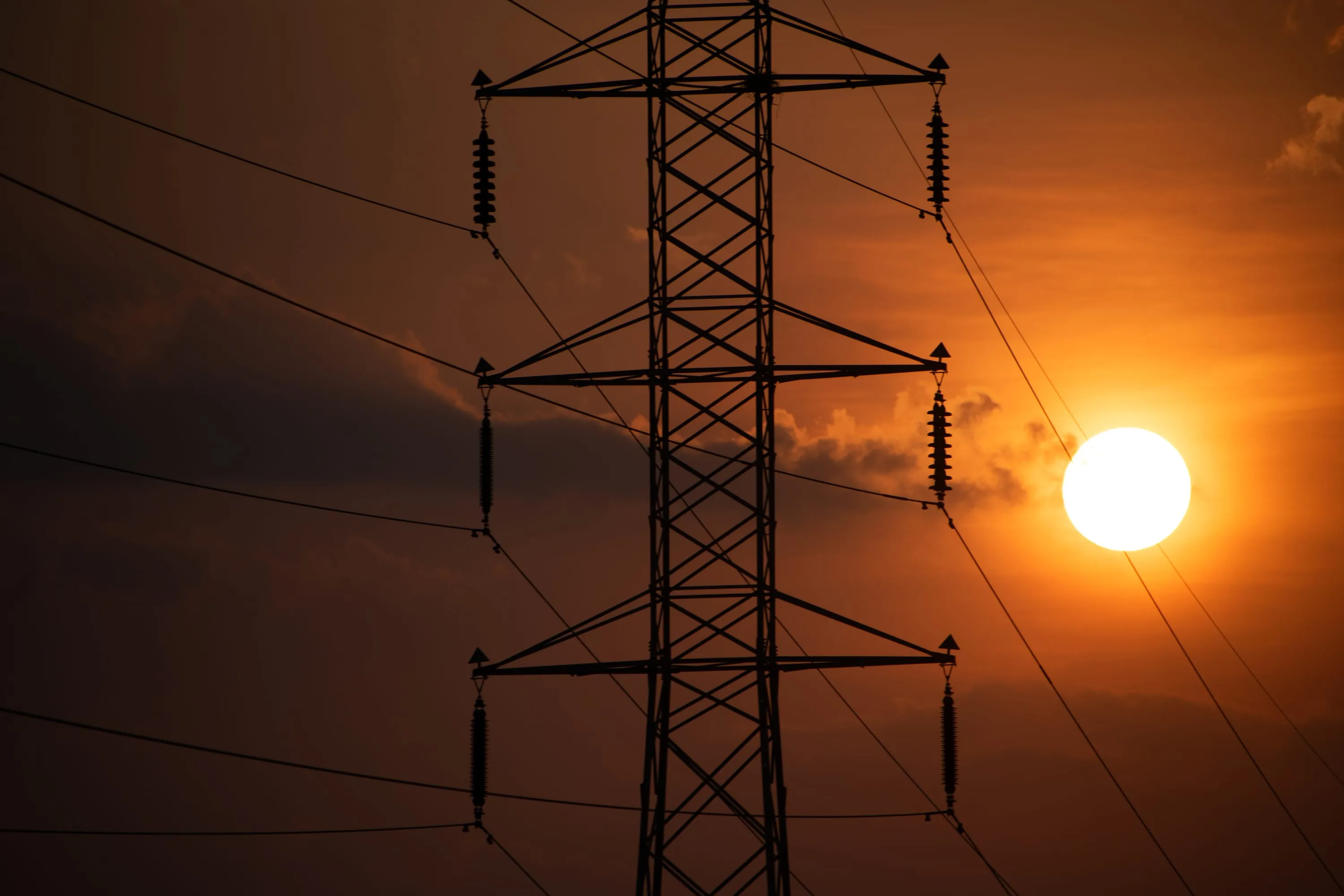 An electricity pylon in silhouette with the setting sun caught in its lattice.