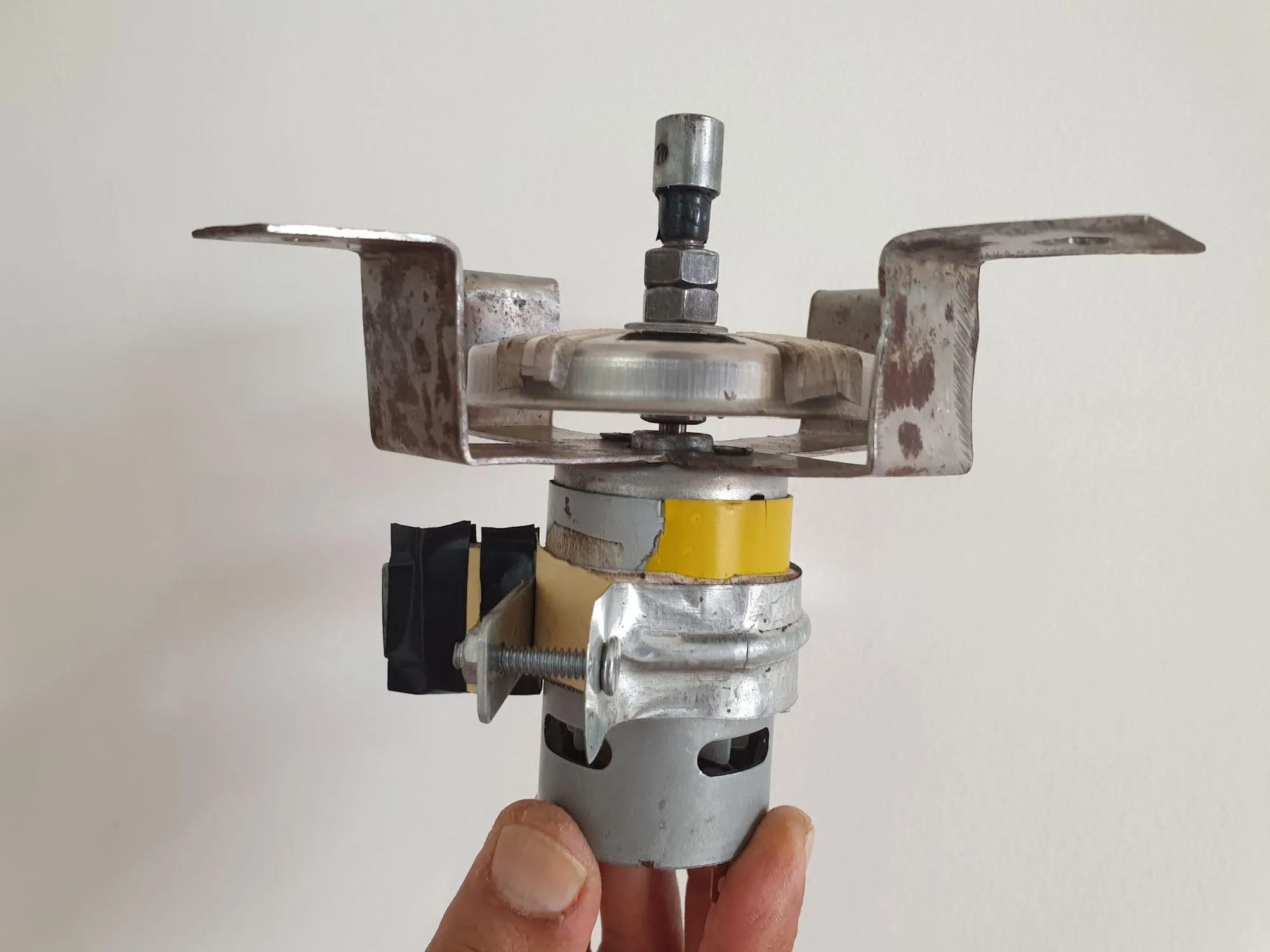 A DC motor held in one hand, fitted with a bent metal clamp carrying two infrared sensor boards either side of a slotted disc on the shaft.
