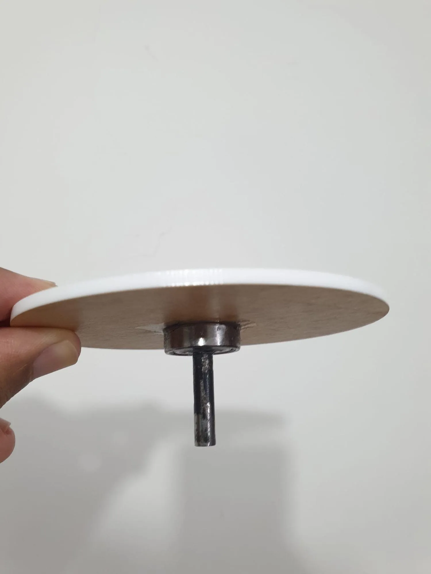A white circular acrylic disc with a short central shaft, held between finger and thumb.