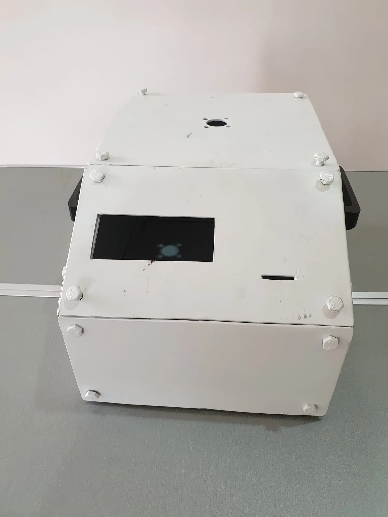 The second version: a bolted sheet-metal box painted white, with a rectangular display window in the sloped front and a bore for the motor shaft on top.